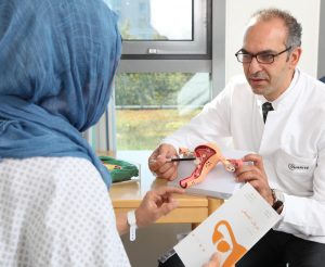 Prof. Dr. med. Dr. h.c. Jalid Sehouli, Charité Berlin, spricht mit einer Patientin mit Kopftuch anhand eines Modelles über Eierstöcke.