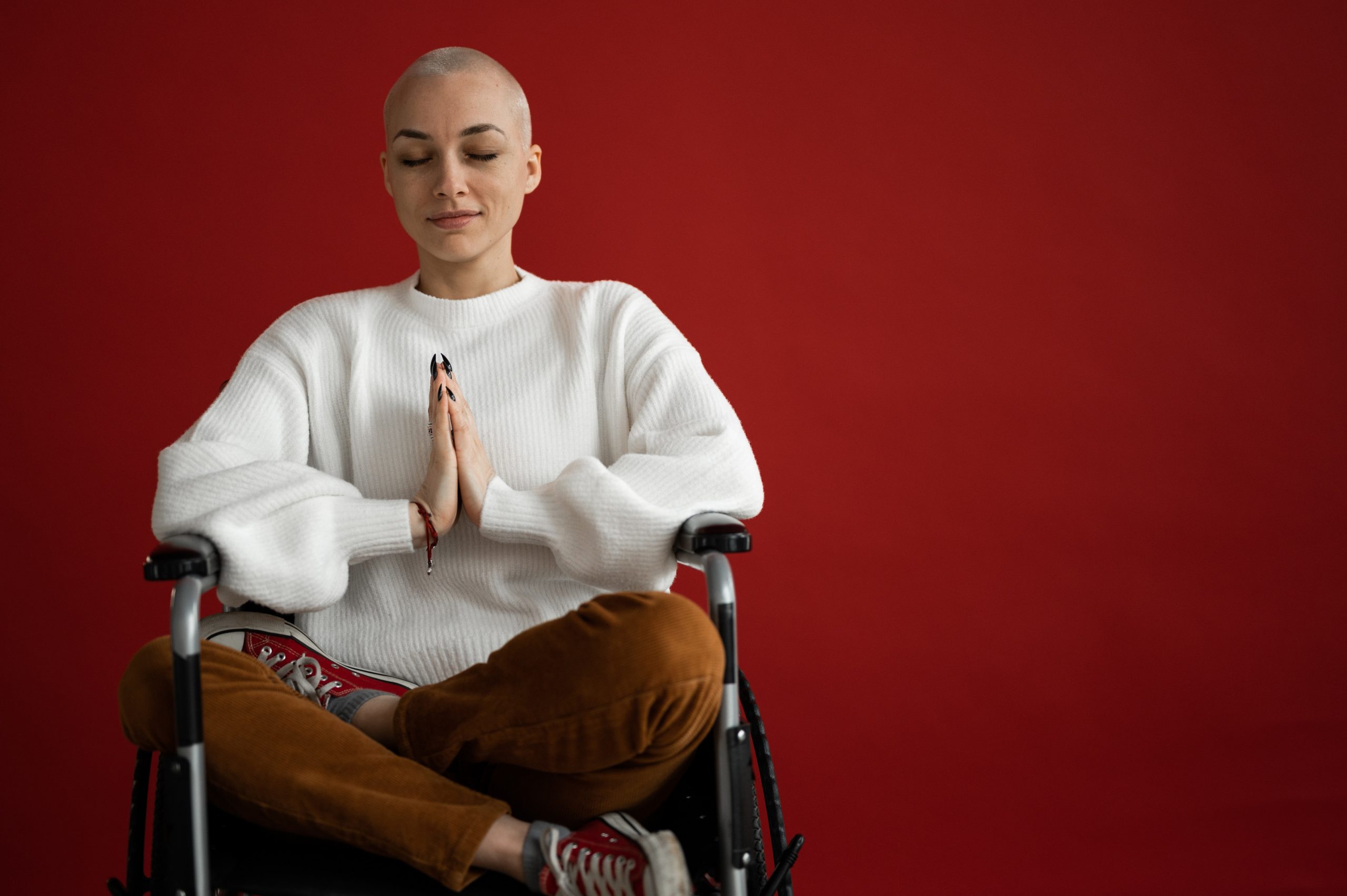 Beitragsbild zum Artikel "Yoga und Krebs" - Junge Frau mit kurzen Haaren meditiert im Rollstuhl